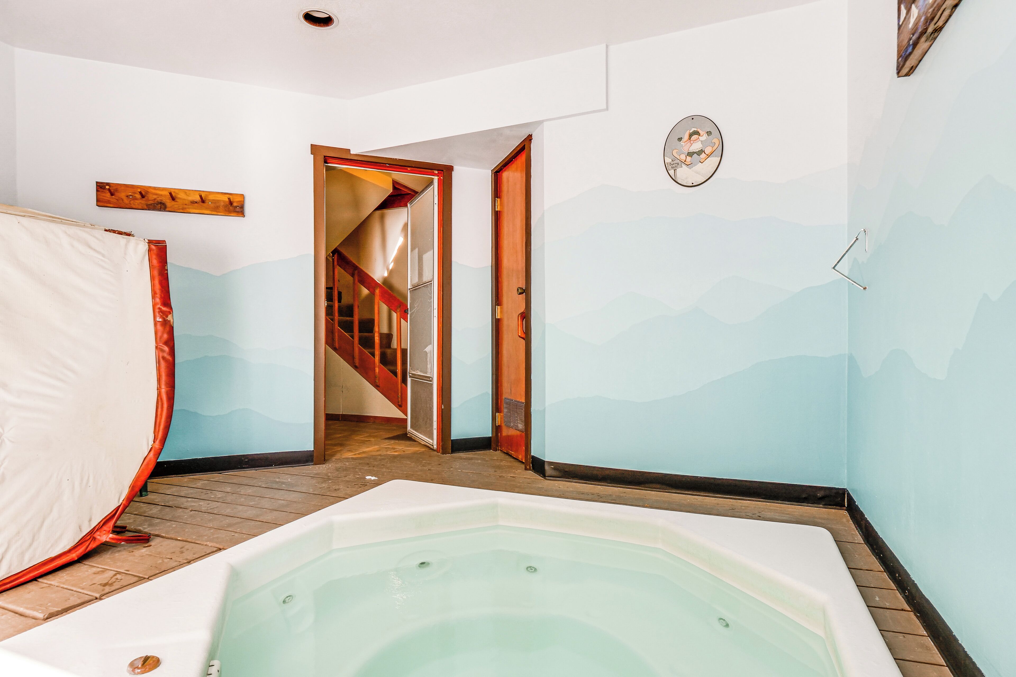 Una habitación con una bañera grande, una escalera de madera y un muro decorado con un diseño de montaña.
