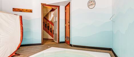 A room with a large bathtub, a wooden staircase, and a wall with a mountain design.