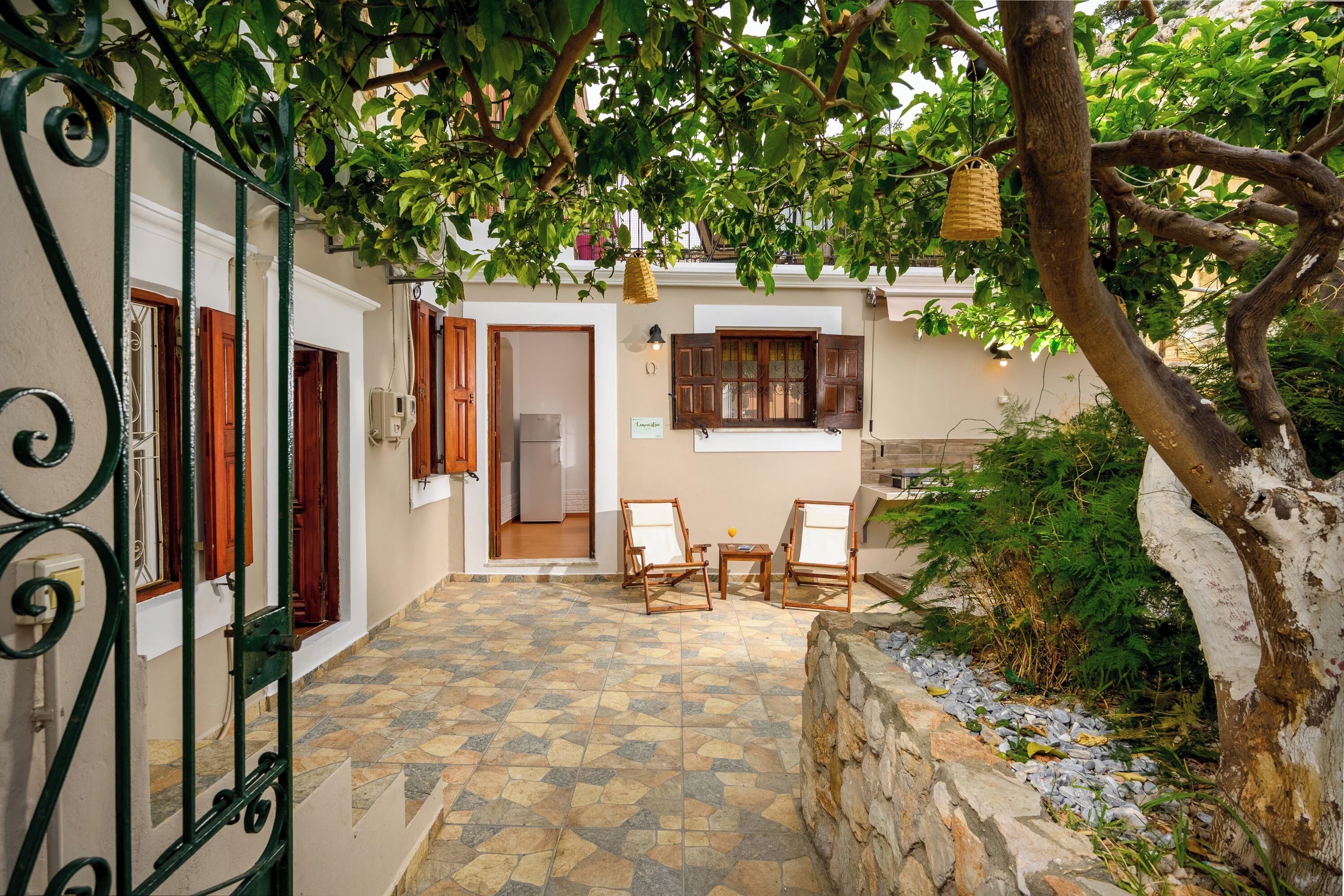 Un cortile con pavimento piastrellato, parete in pietra e tavolo in legno con sedie.