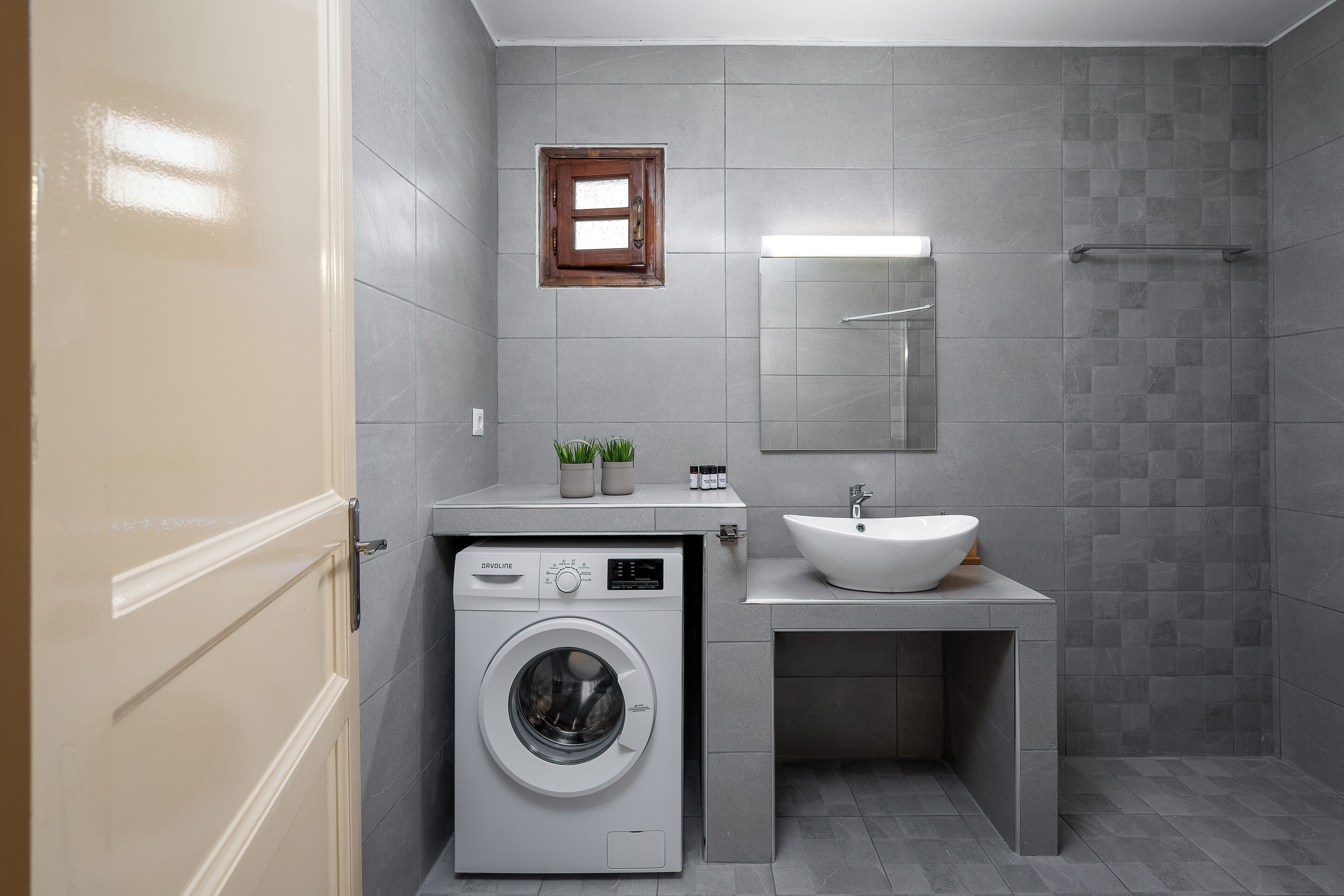 Une salle de bain moderne équipée d’un lave-linge, d’un lavabo et d’une petite fenêtre.