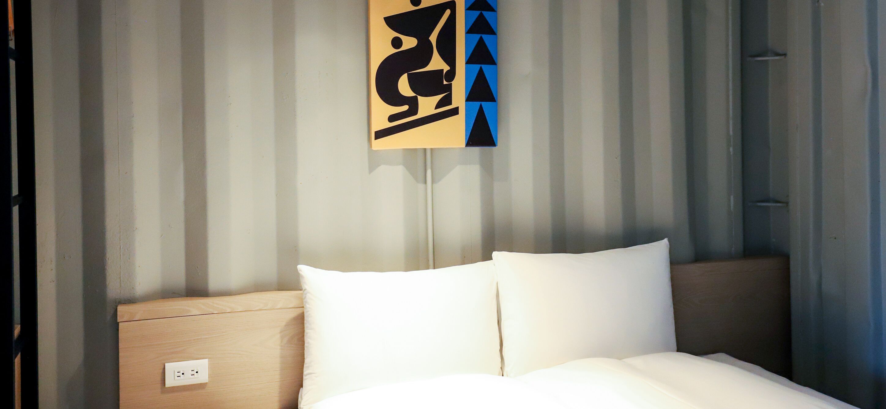 A hotel room with a bed, a wooden headboard, and a wall-mounted artwork.