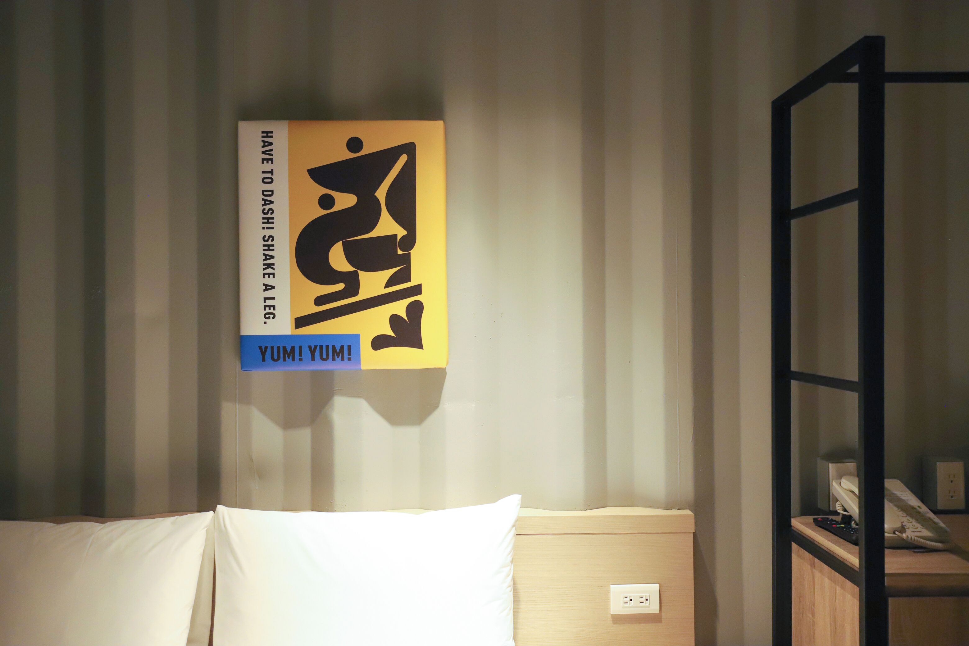 Una camera d'albergo con un letto, un comodino, una mensola e una parete con un cartello.