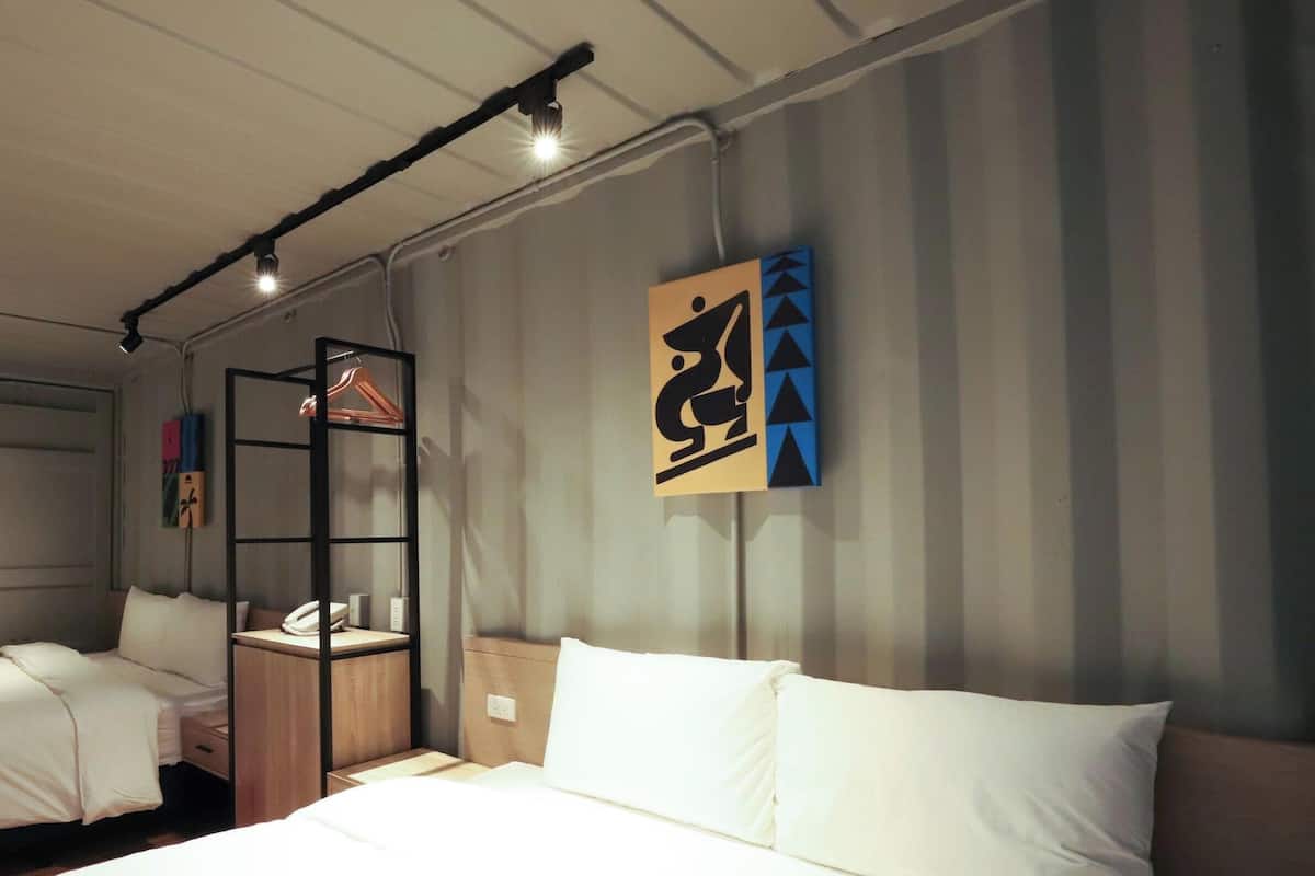 A hotel room with a bunk bed, a wardrobe, a bedside table, and a wall-mounted artwork.