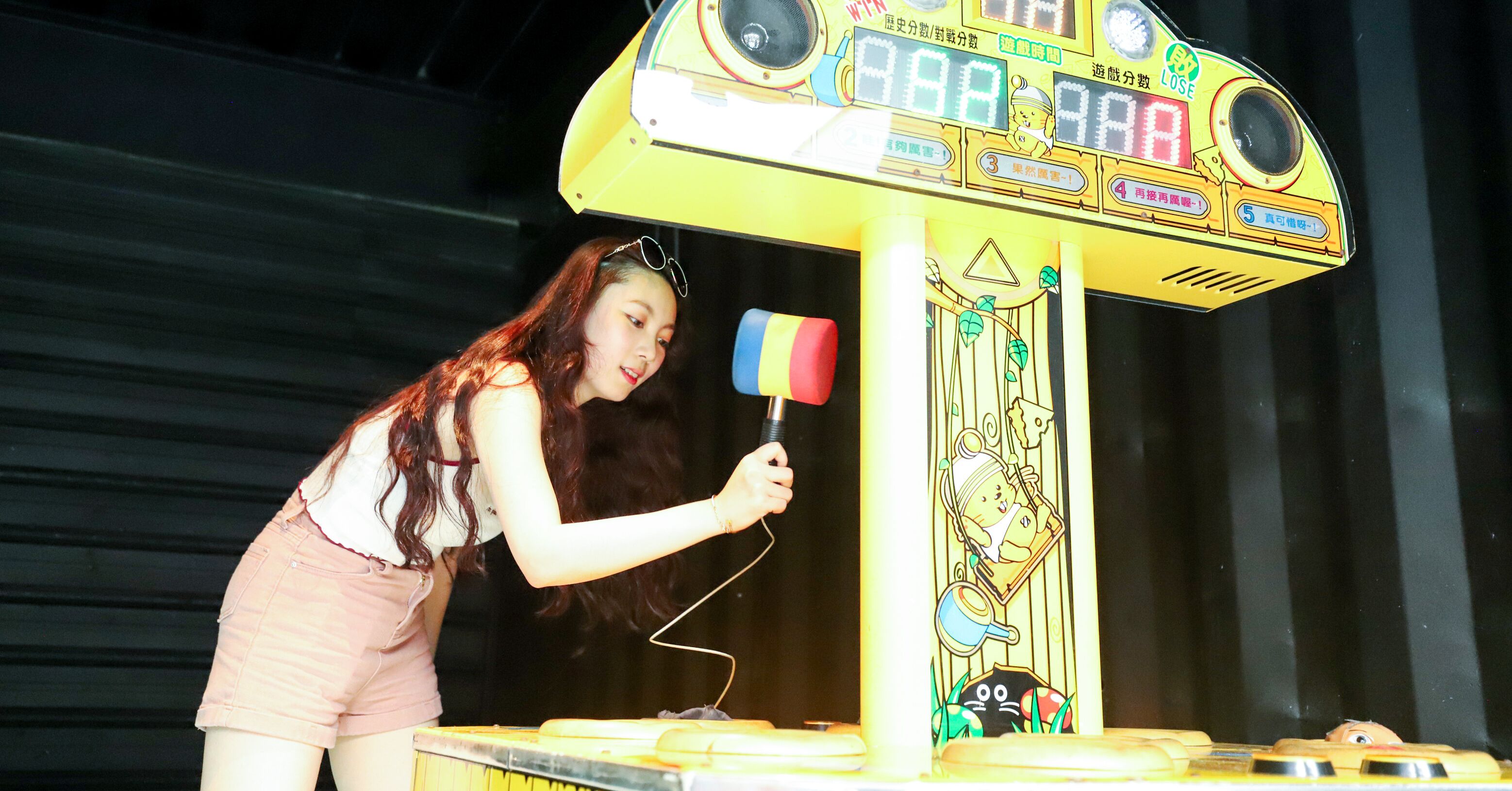A person playing a game at a yellow arcade machine with cartoon characters.
