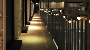 Un pasillo con varias puertas a un lado y una barandilla con luces al otro.