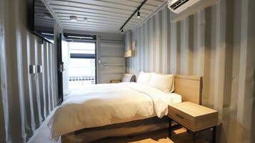 A modern hotel room with a bed, bedside table, and built-in air conditioning unit.