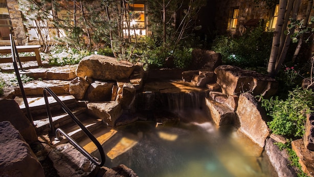 A stone water feature with a small waterfall, surrounded by rocks and greenery. - River Club 304 3 Bedroom Condo by Alpine Lodging Telluride (Telluride)