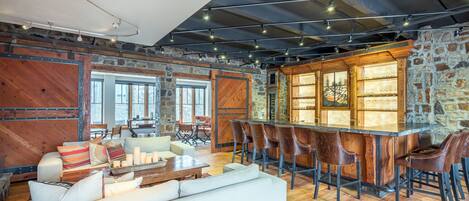 A spacious living area with a large wooden bar, leather chairs, and a white sofa.