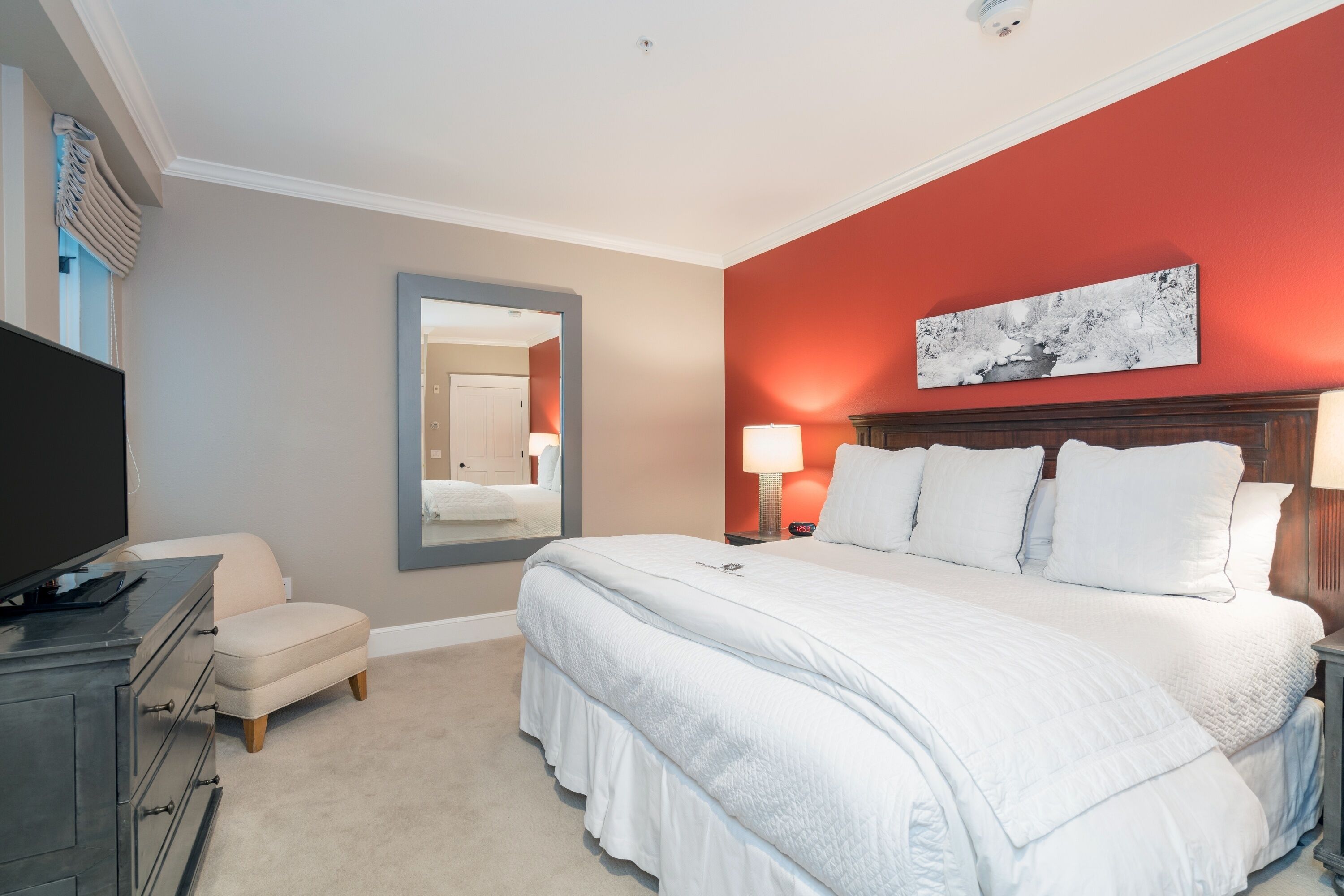 A hotel room with a large bed, a TV, a desk, and a mirror.