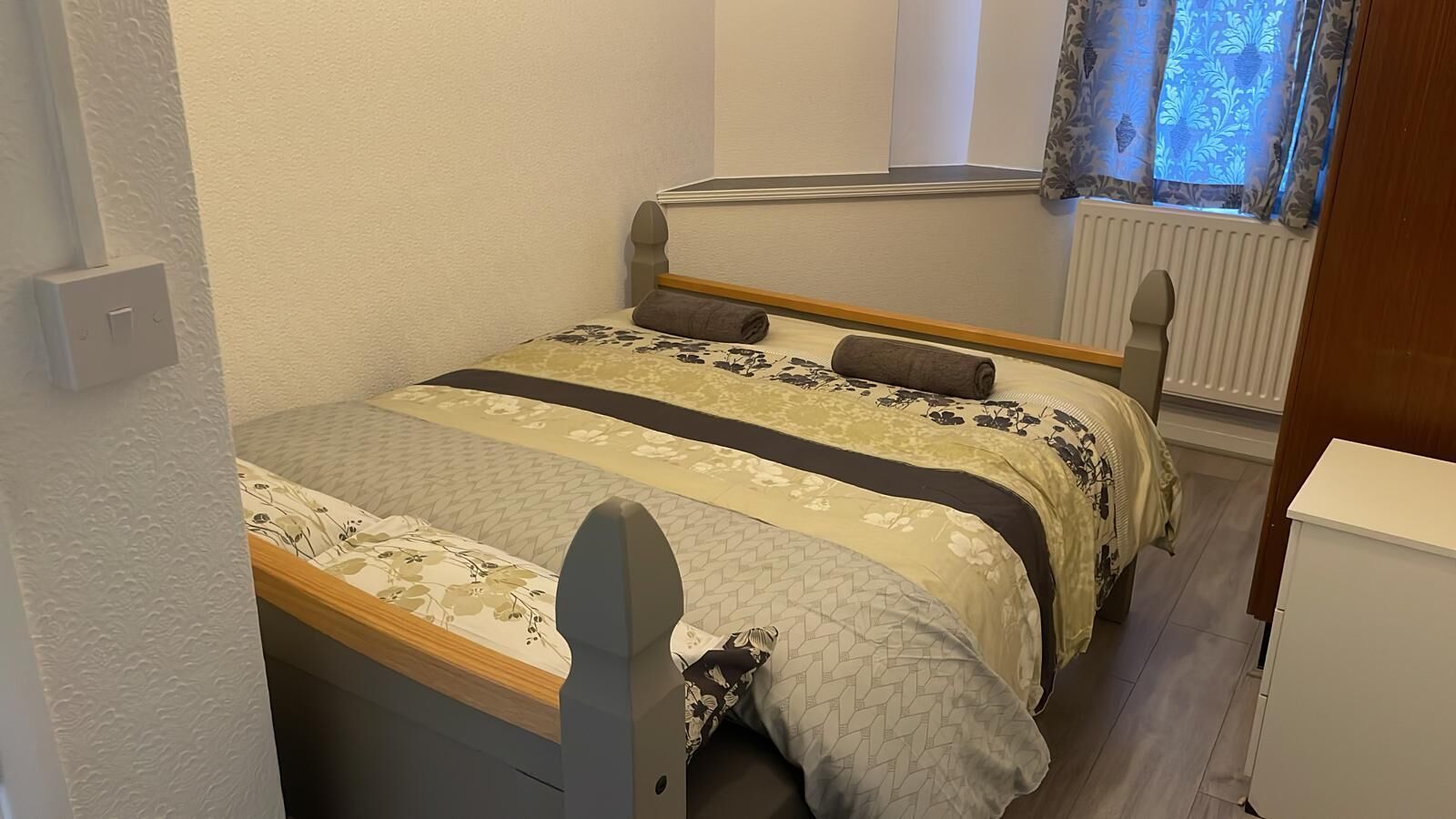 A small, neatly arranged bedroom with a bed, a nightstand, and a radiator.