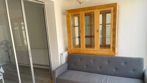 Un canapé gris, un meuble en bois et une porte-fenêtre coulissante dans une pièce dont le sol est recouvert de carreaux.