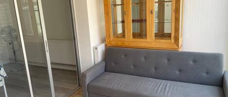A grey sofa, a wooden cabinet, and a sliding glass door in a room with tiled flooring.