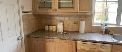 A kitchen with wooden cabinets, a granite countertop, a Bosch dishwasher, and a window with a view of buildings.