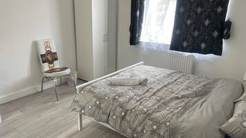 Une chambre à coucher avec un lit, une armoire, une chaise et une fenêtre avec des rideaux.