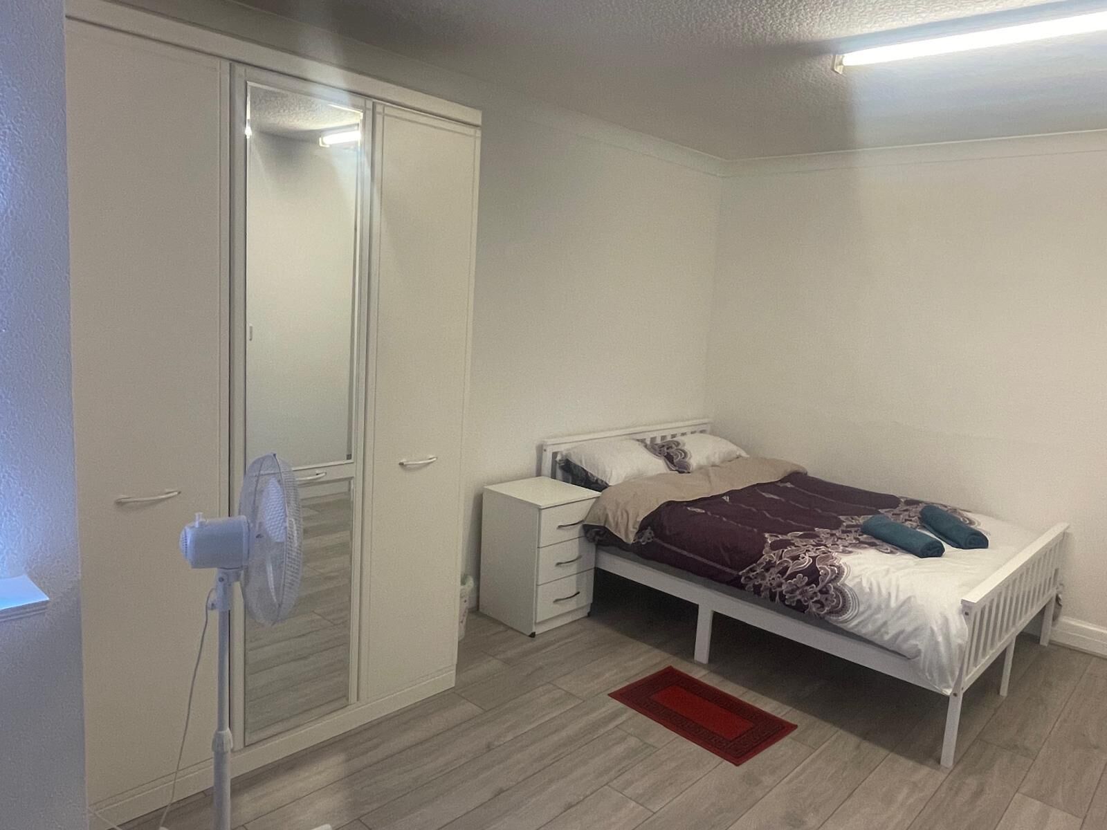 A bedroom with a bed, a wardrobe, a bedside table, and a red rug.