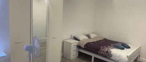 A bedroom with a bed, a wardrobe, a bedside table, and a red rug.