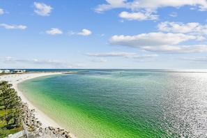 Ein Küstenstrand mit klarem türkisblauem Wasser, einem Sandstrand und einem in der Ferne liegenden Pier.