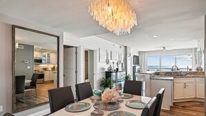 Une cuisine moderne avec vue sur l’océan, un coin repas agrémenté d’un grand miroir et un lustre.