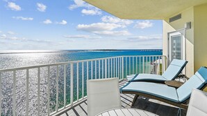 Un balcon avec deux fauteuils de jardin, une vue sur l’océan et un quai situé au loin.