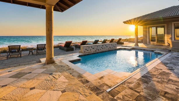 A poolside area with lounge chairs and a view of the ocean at sunset.