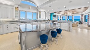 A spacious kitchen with a large island, white cabinetry, and a view of the ocean.