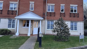 Un immeuble résidentiel à plusieurs étages, doté d’une façade en briques, de fenêtres à cadre blanc et d’un petit hall d’entrée avec une porte blanche.
