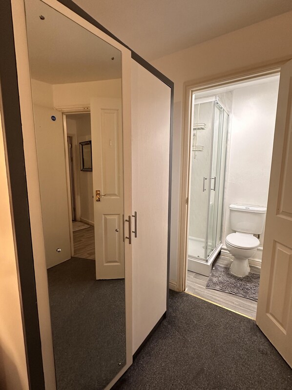 A bathroom with a glass shower enclosure, a toilet, and a door leading to another room.