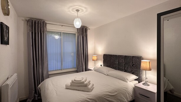 Une chambre à coucher avec un lit, deux lampes de chevet, une fenêtre avec des rideaux, un radiateur et une porte.