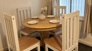 Un coin repas avec une table ronde en bois, quatre chaises blanches et un vase rempli de fleurs.