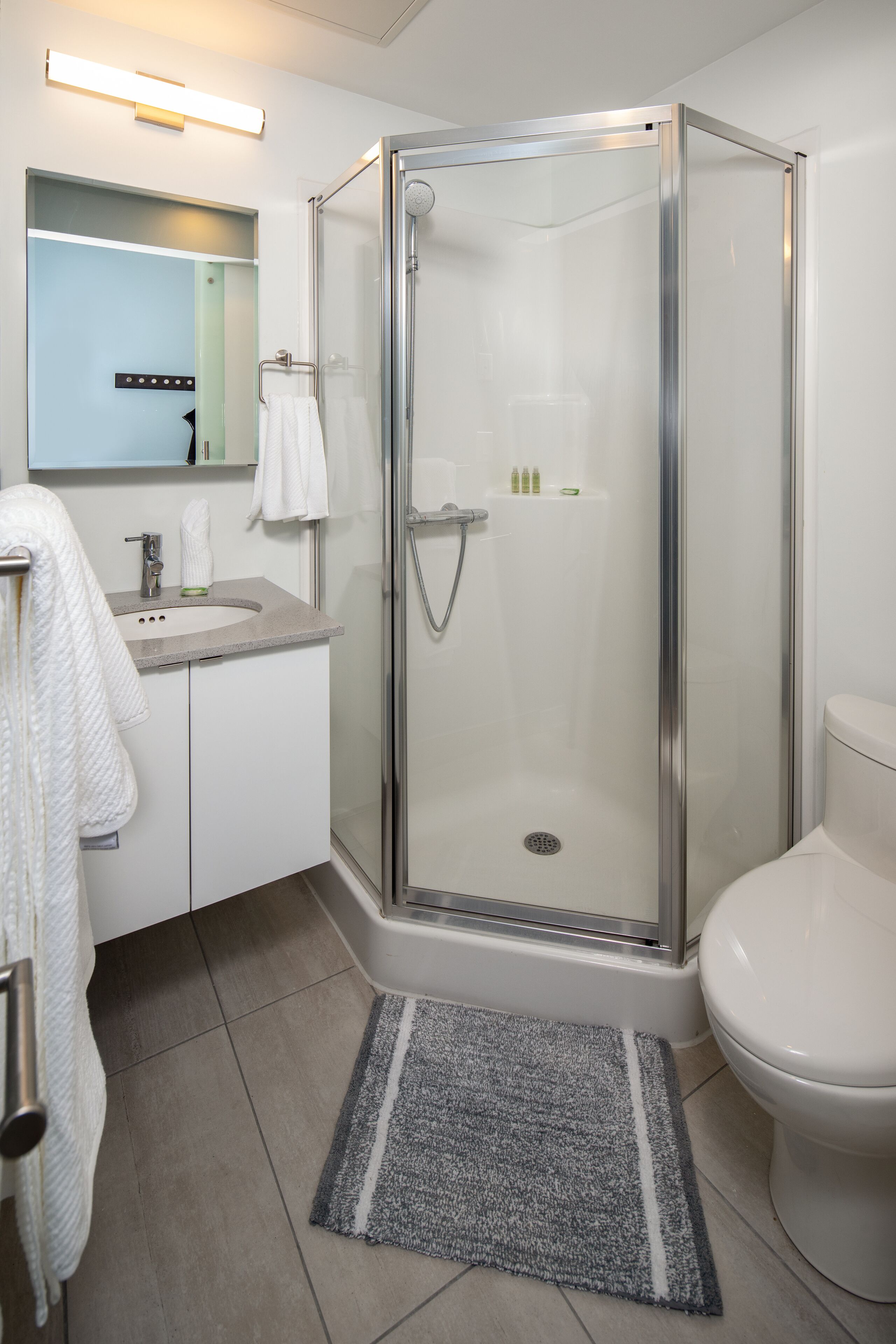 Ein modernes Badezimmer mit einer gläsernen Duschkabine, einer weißen Toilette, einem Waschbecken mit Spiegel darüber und einem Handtuchhalter.