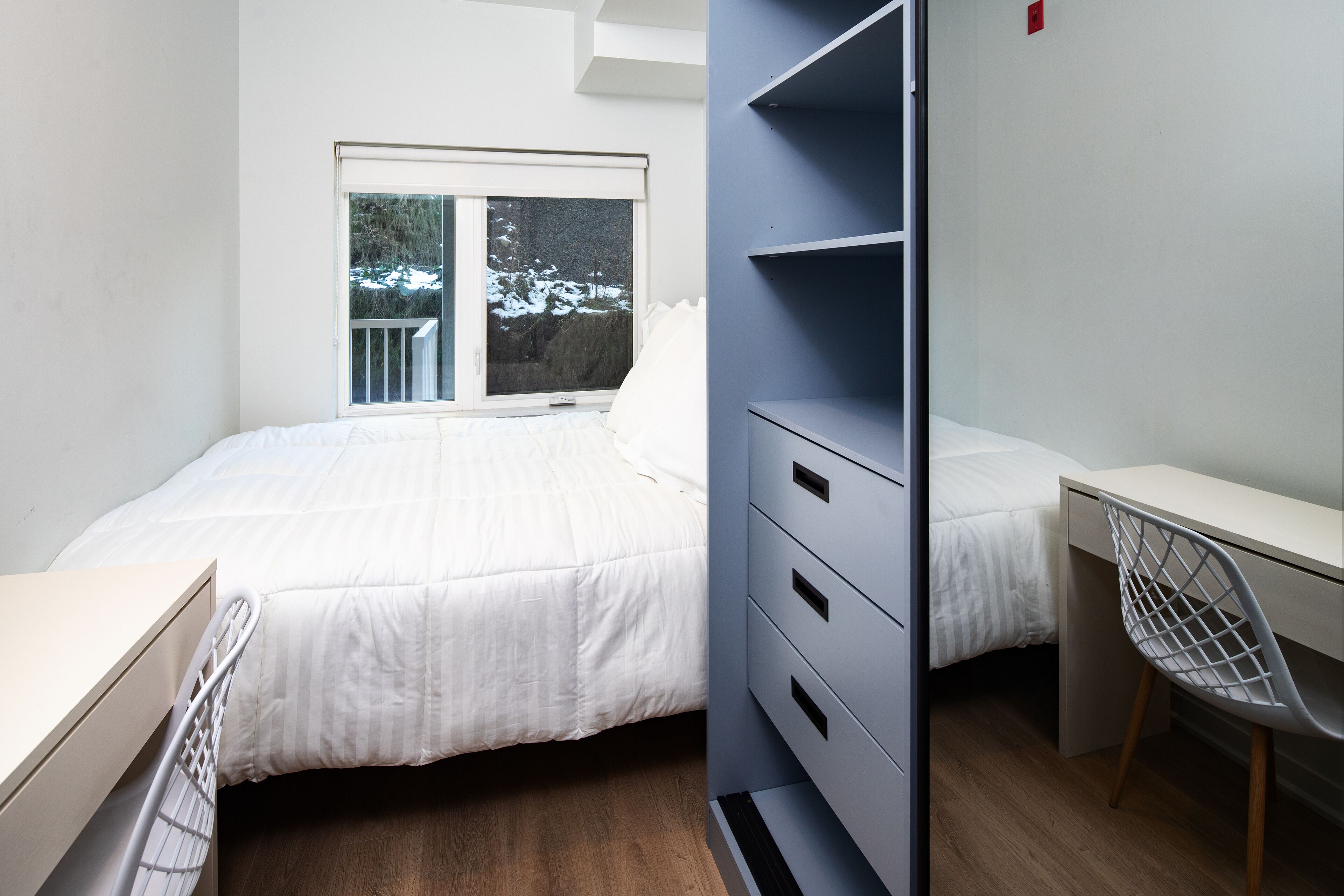 Un dormitorio con cama, escritorio y silla. Se ve nieve a través de la ventana.