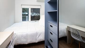 A bedroom with a bed, a desk, and a chair. There is a window with a view of snow outside.