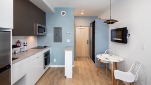 Een moderne keuken met witte kasten, een magnetron en een inbouwoven. Er is een klein eethoekje met een witte tafel en stoelen.