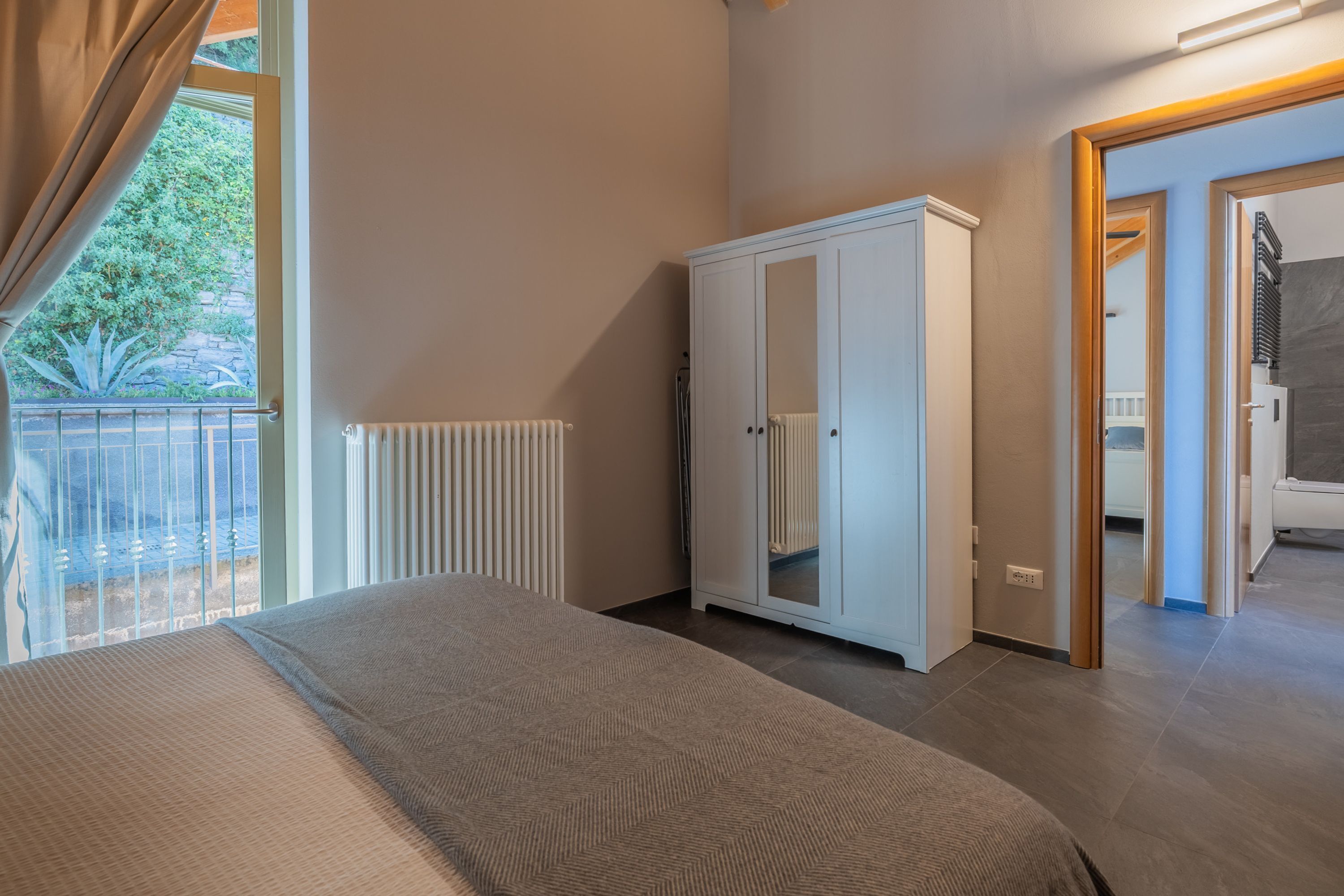 A bedroom with a large bed, a wardrobe, a radiator, and a view of the outdoors.