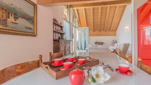A cozy room with a wooden ceiling, a painting on the wall, and a dining area with red cups and saucers. - Veloccino del Lago in Perledo (Perledo)