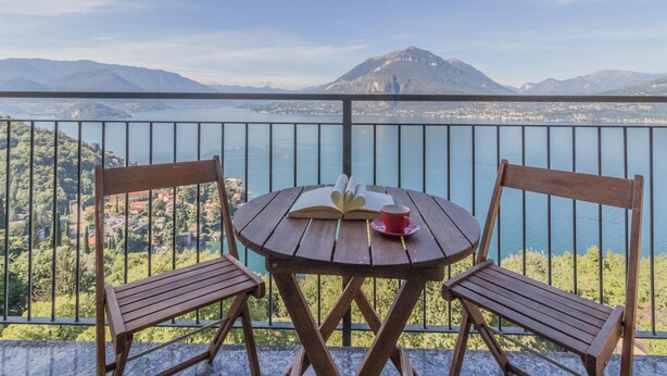 A balcony with two wooden chairs and a round table, overlooking a lake with mountains in the background. - Veloccino del Lago in Perledo (Perledo)