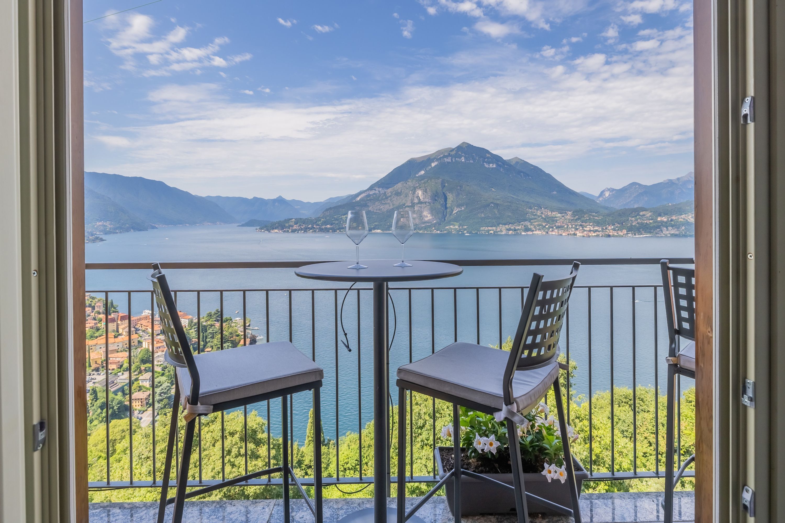 Een balkon met twee stoelen en een tafel, met uitzicht op een meer en bergen.