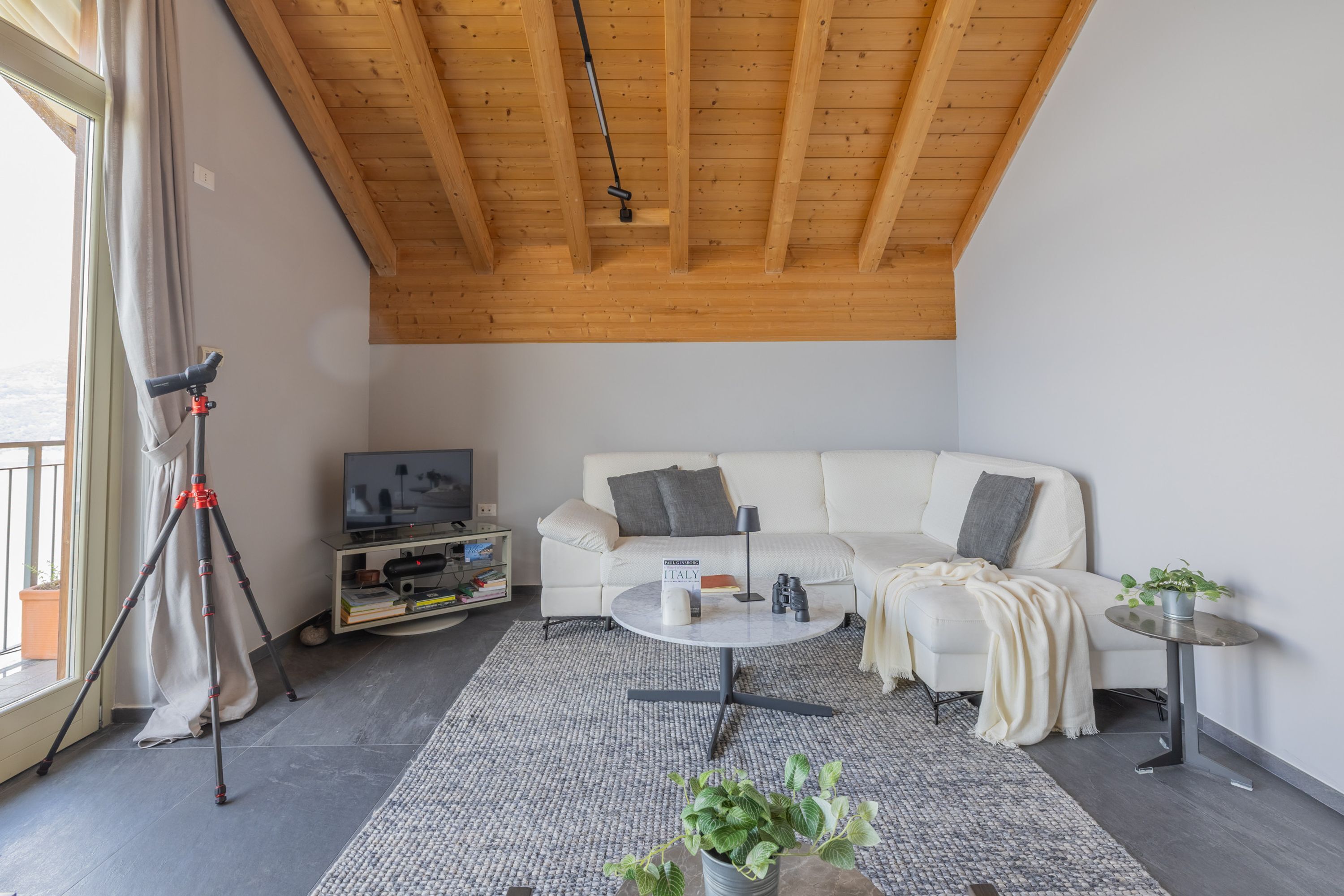 En moderne stue med en hvid sofa, et sofabord og et fjernsyn. Der er et stativ og en potteplante på gulvet.