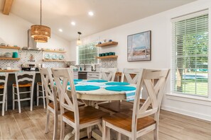 A modern kitchen with white cabinetry, a central island with blue placemats, and wooden chairs. - Modern Ground-Level Vacation Home, Centrally Located on Dauphin Island - Las Bri (Dauphin Island)