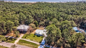 An aerial view of a residential area with houses surrounded by dense forest, a road, and a beach in the background. - Modern Ground-Level Vacation Home, Centrally Located on Dauphin Island - Las Bri (Dauphin Island)