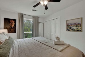 A bedroom with a bed, a ceiling fan, a window with curtains, and two paintings on the walls.