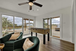 Amplia habitación con mesa de fútbol de mesa, dos sillones verdes y un ventilador de techo.