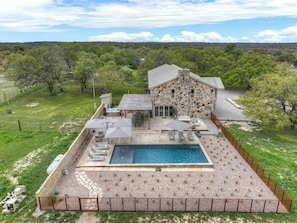 Una casa de piedra con piscina, rodeada por un patio cercado con sillones y sombrillas.