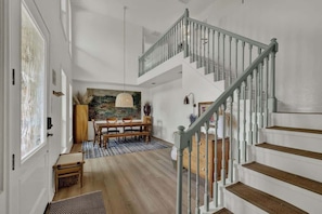 Un interior espacioso con una escalera, un comedor y un cuadro grande en la pared.
