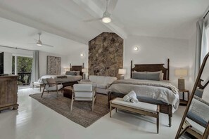 A spacious bedroom with a large bed, a seating area with chairs, a stone accent wall, and a balcony with a view.
