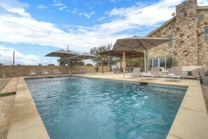 A swimming pool with lounge chairs and umbrellas, surrounded by stone walls and a stone building. - Grasslands: Pool+Hot-Tub+Views on 290 Wine Trail! (Johnson City)