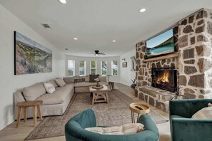 A living room with a stone fireplace, a large TV mounted above it, a sofa, and a green armchair.