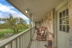 A porch with wooden rocking chairs and a colorful umbrella, overlooking a grassy area with trees.