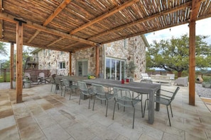 An outdoor patio with a stone wall, wooden pergola, and a long dining table with chairs.