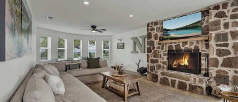 A living room with a stone fireplace, a large window, and a sofa.